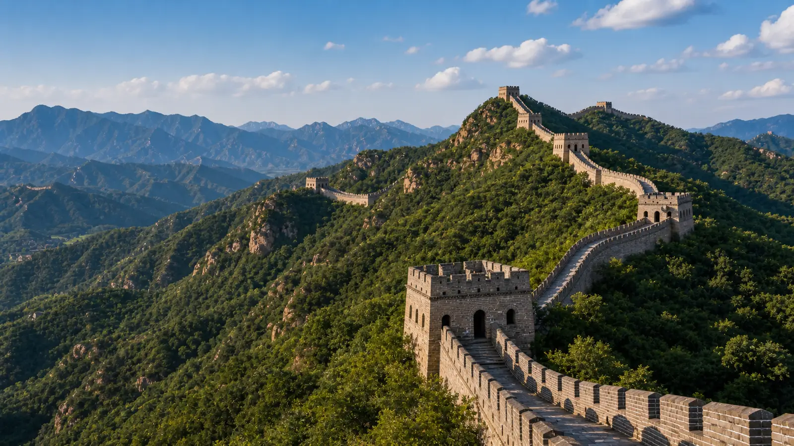 Watchtowers of the Great Wall winding along a forested mountain ridge under a clear sky north of Beijing